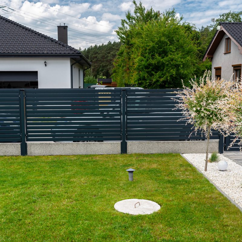 A modern panel fence in anthracite color, a visible sliding gate to the garage and a wicket with