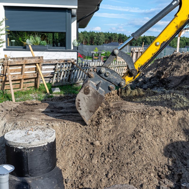 Using an excavator to bury a 10 m3 concrete septic tank located in the garden next to the house.